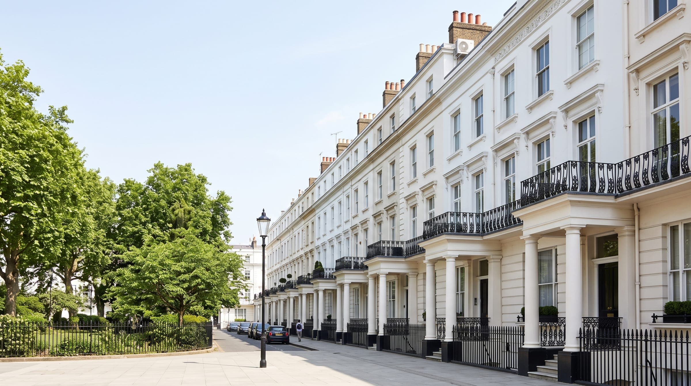 White stucco terraced houses with columned porches and iron balconies facing a leafy garden square in central London