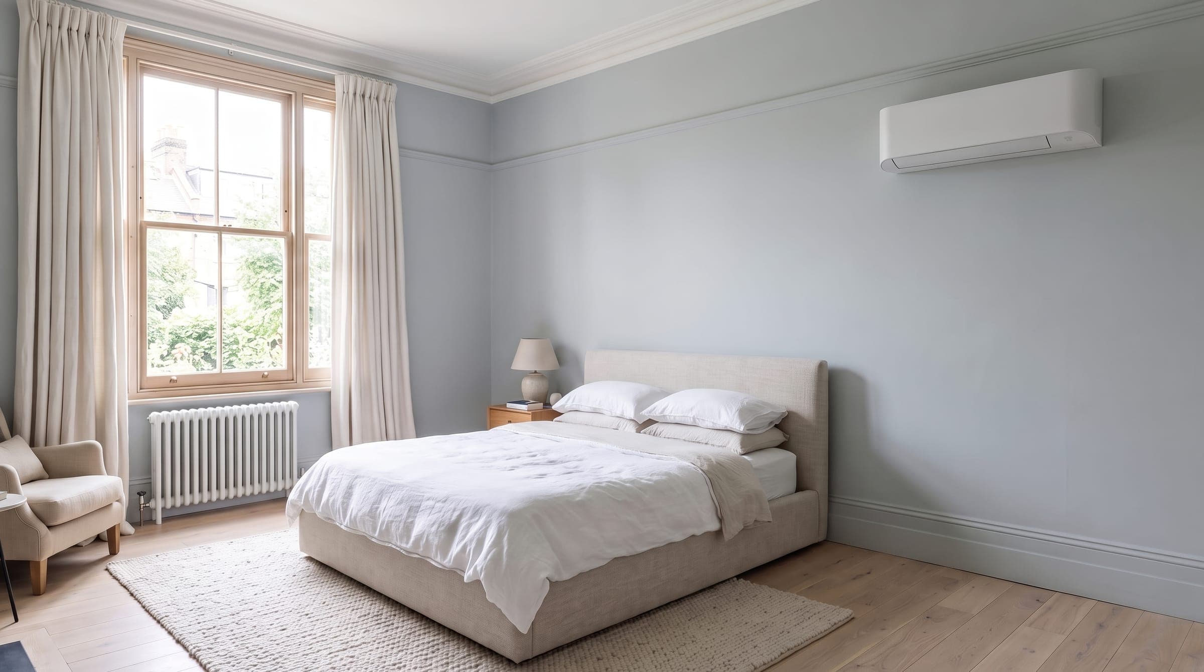 Calm main bedroom with pale blue walls and a white air conditioning unit high on the wall