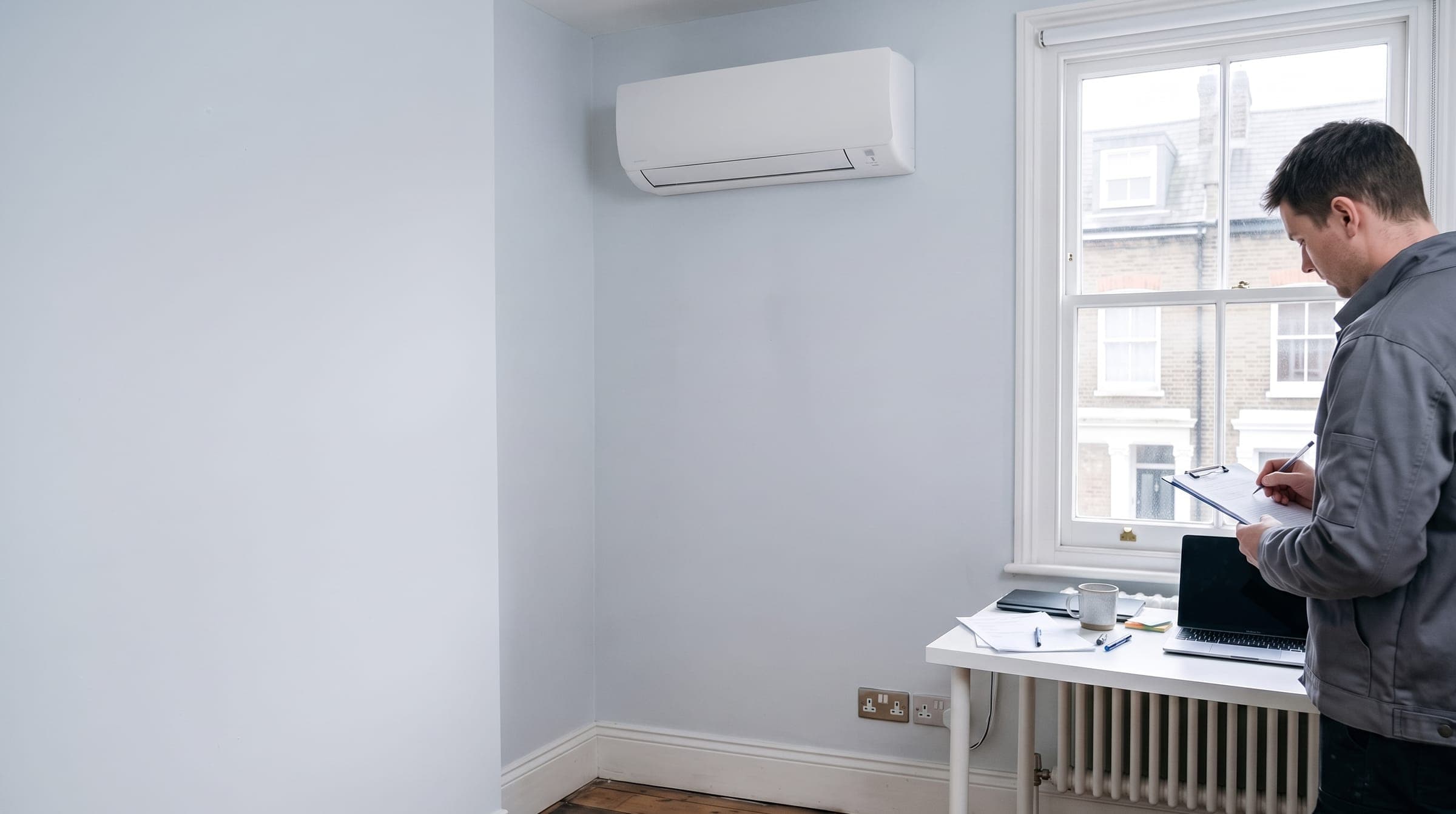 Engineer writing up a service record beside a wall-mounted air conditioning unit in a London home office