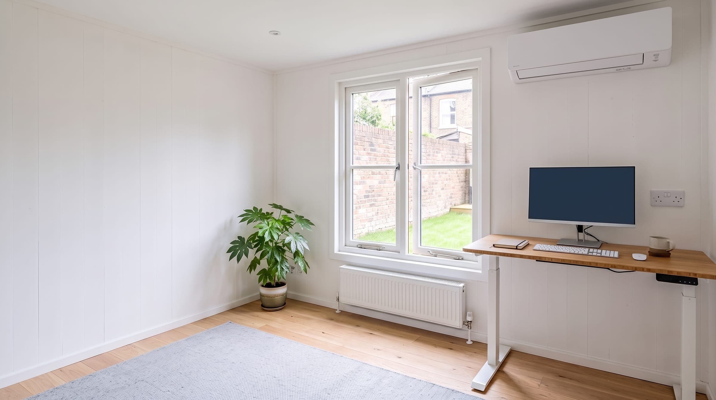 White wall-mounted air conditioning unit in a bright garden office at the end of a London garden