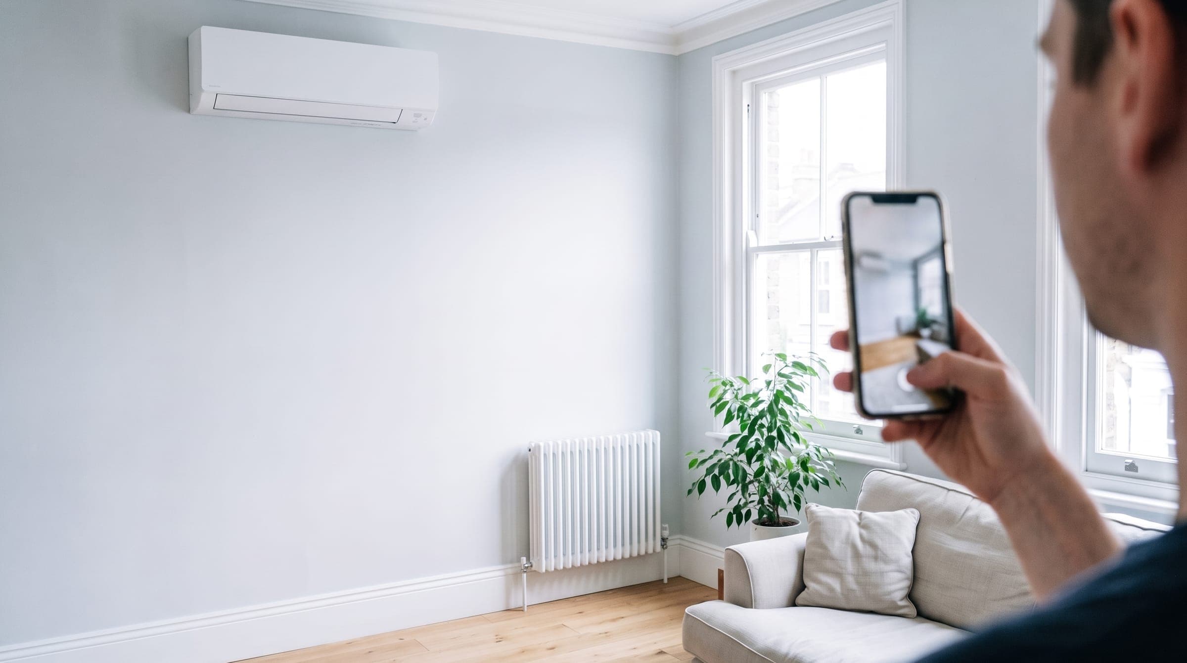 Person taking a photo on their phone of a bright room with a white wall-mounted air conditioning unit