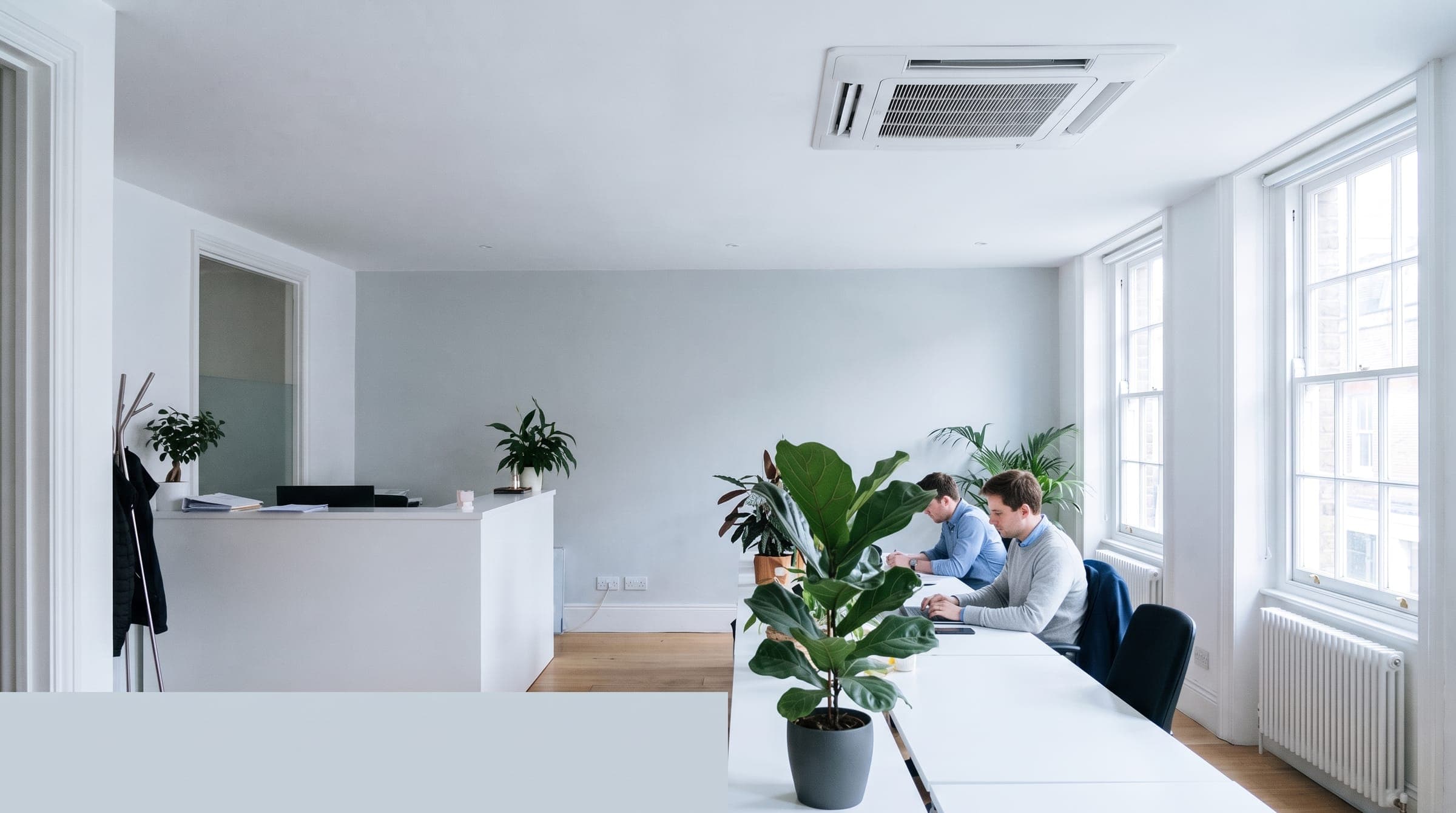 Small open-plan office with a white ceiling cassette air conditioning unit above the desks