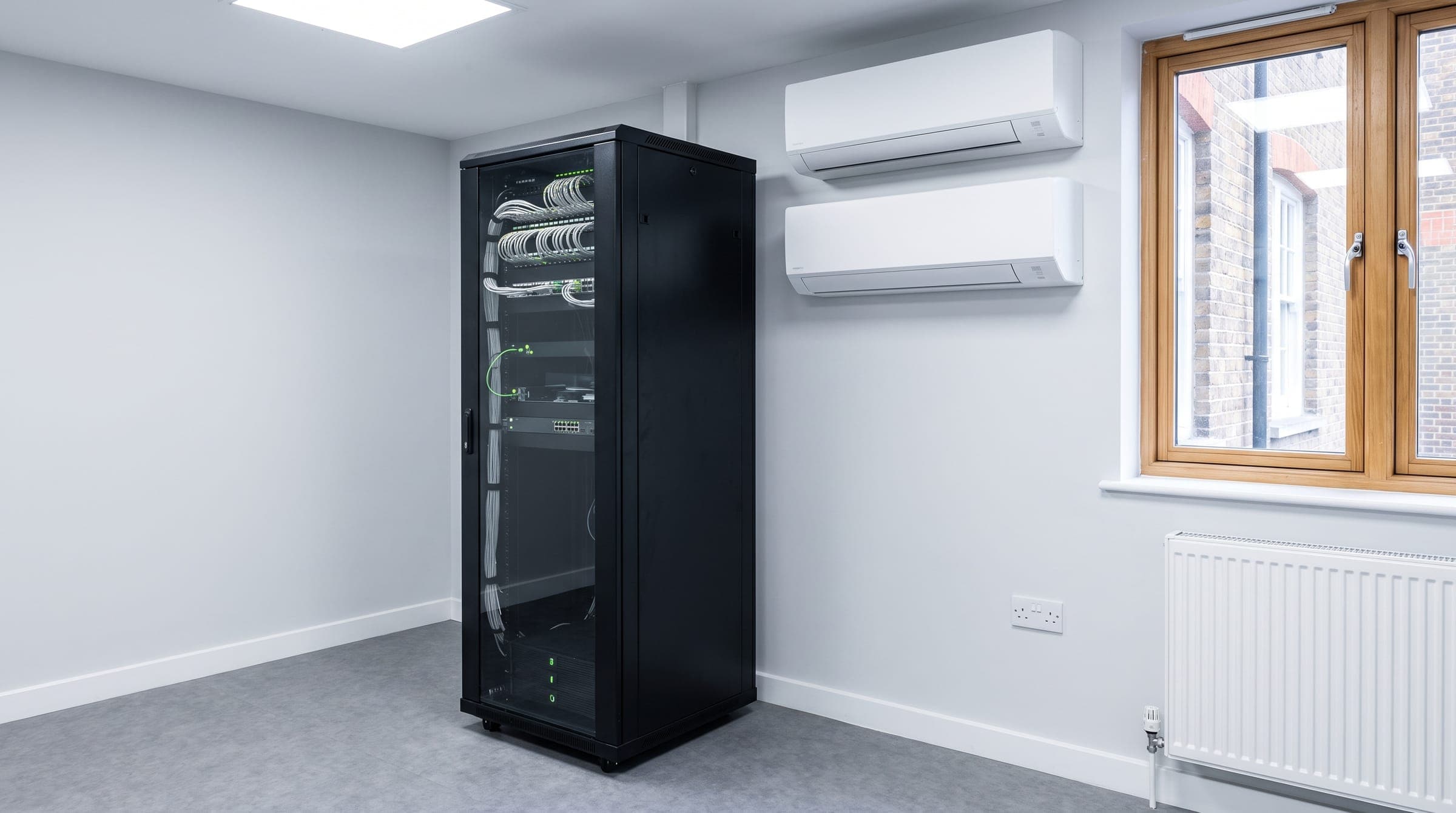 Small comms room with a network cabinet and two wall-mounted air conditioning units, one on standby