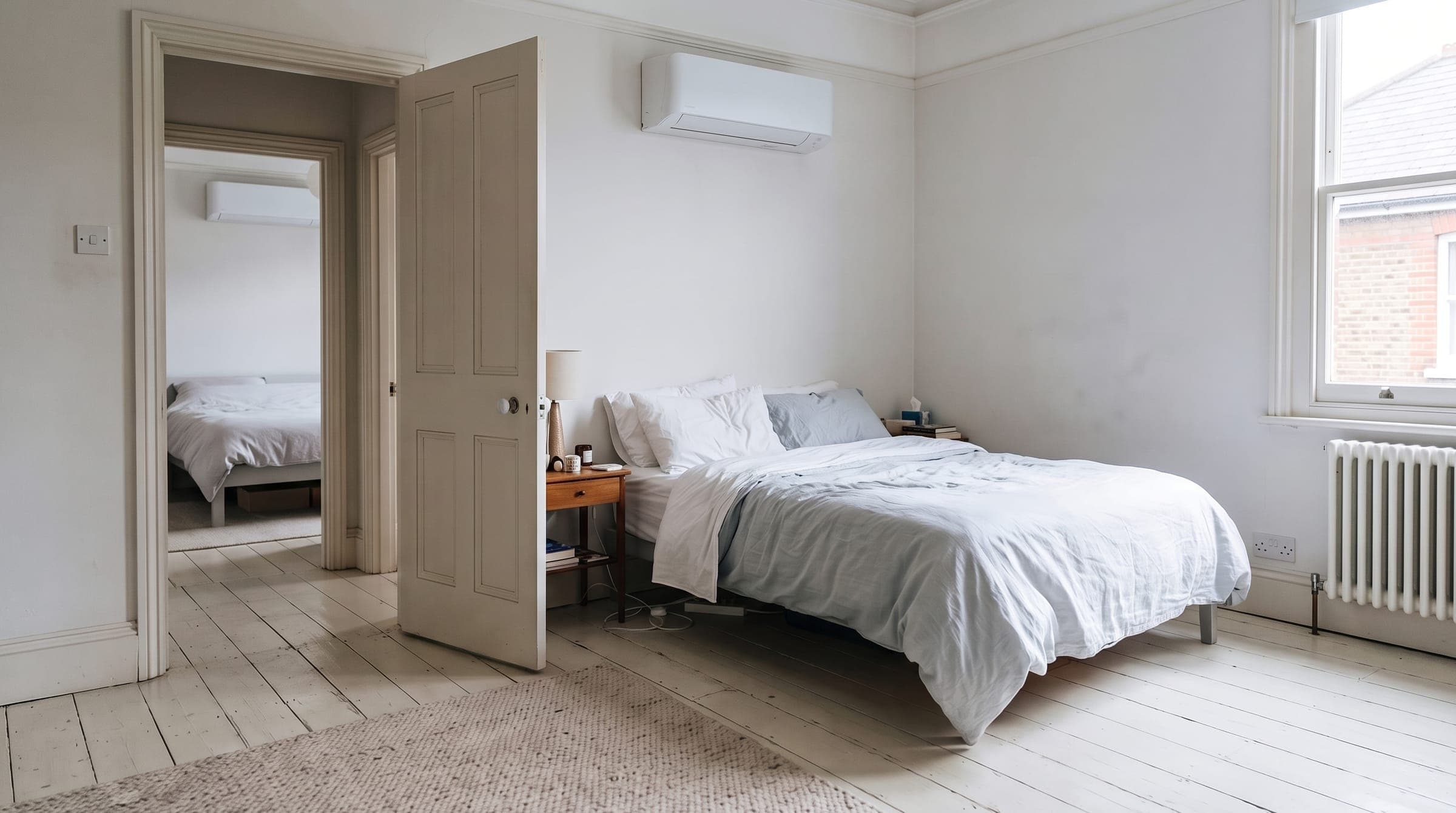 White wall-mounted air conditioning unit high on the wall of a calm London bedroom, one room on a multi-split system